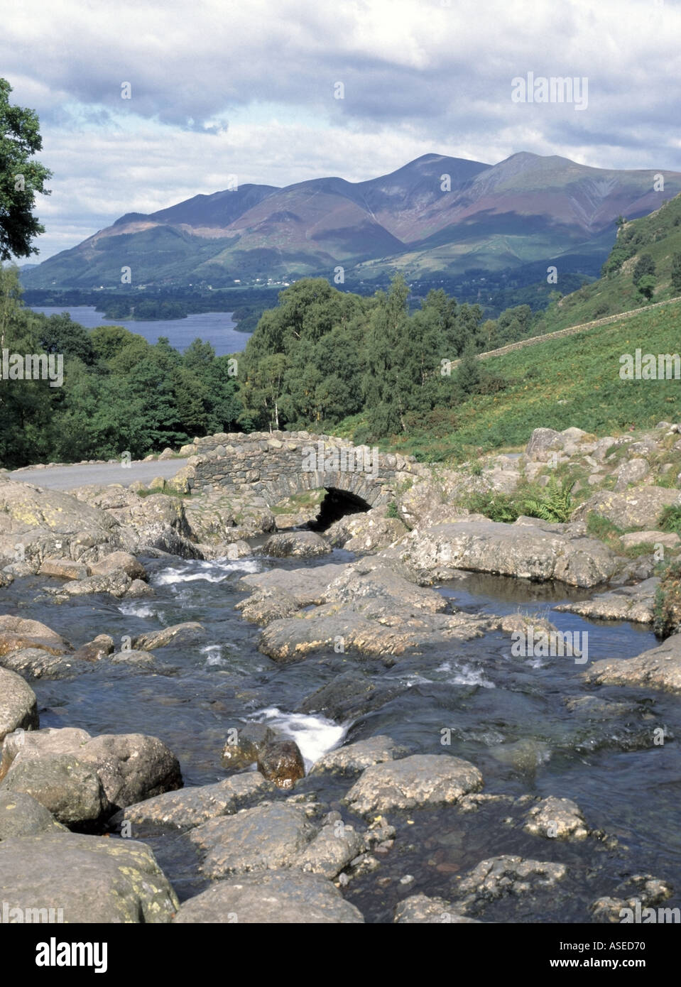 Ashness stone Bridge on single track road over fast flowing stream landscape to Borrowdale towards Derwent Water & Skiddaw Keswick Cumbria England  UK Stock Photo