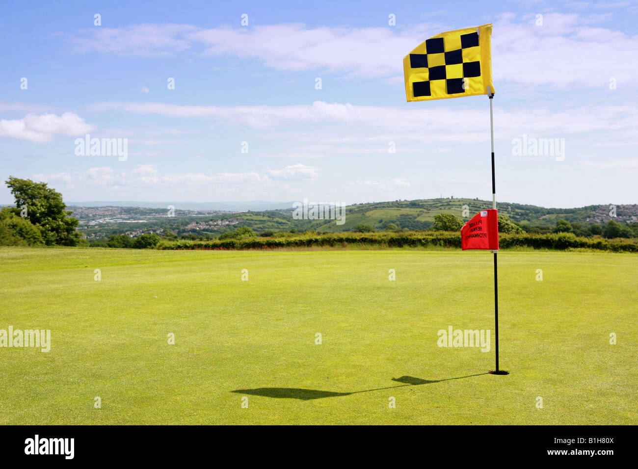 Closeup of golf course putting green hole pin with bright yellow and black chequered flag and luscious green grass golfing image Stock Photo