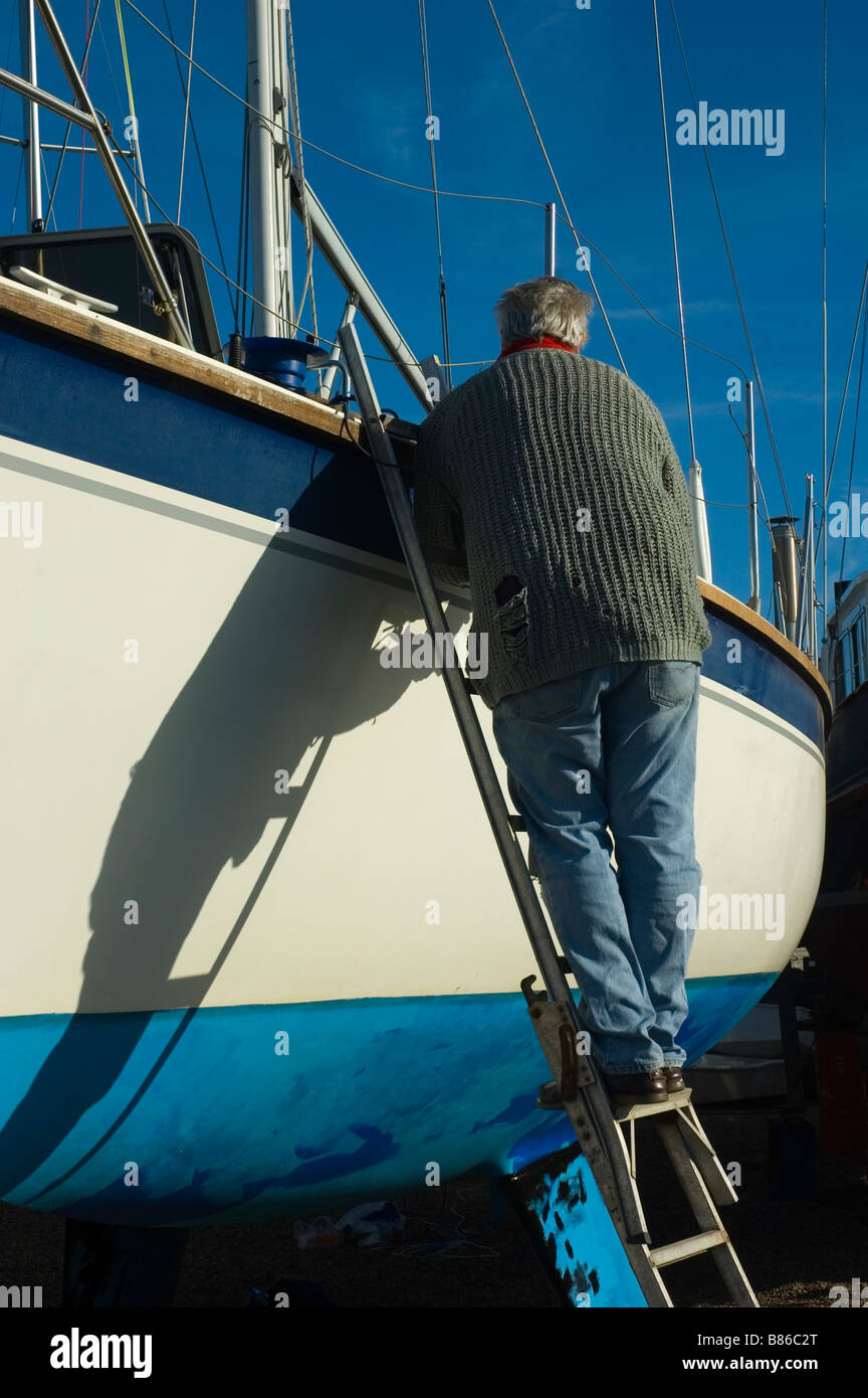 a boat owner carries out old fashioned maintenance and repair work by hand to his yacht in Guernsey harbour. Stock Photo