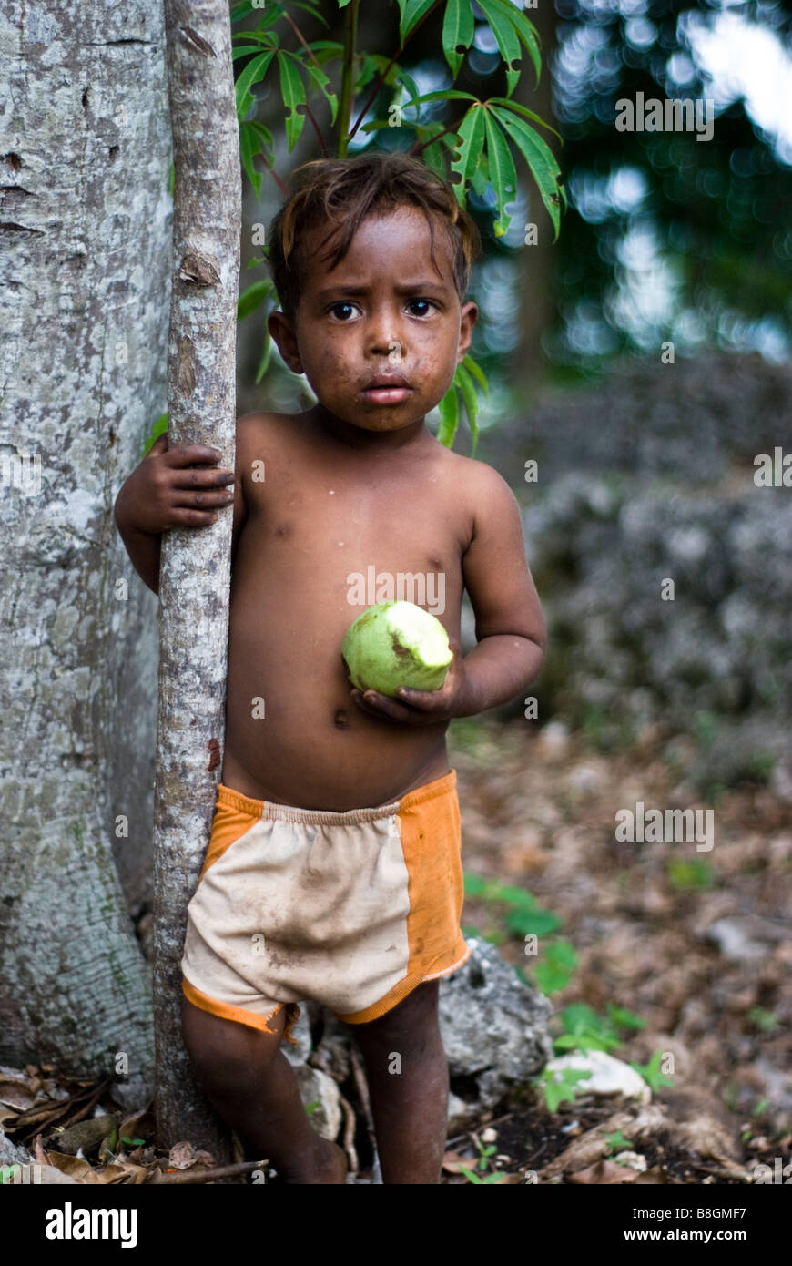 Child eating fruit by tree in the traditional village of None, West Timor, Indonesia Stock Photo