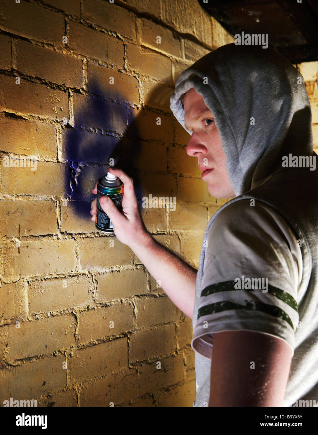 Young hoodie sprays his graffiti tag onto wall Stock Photo