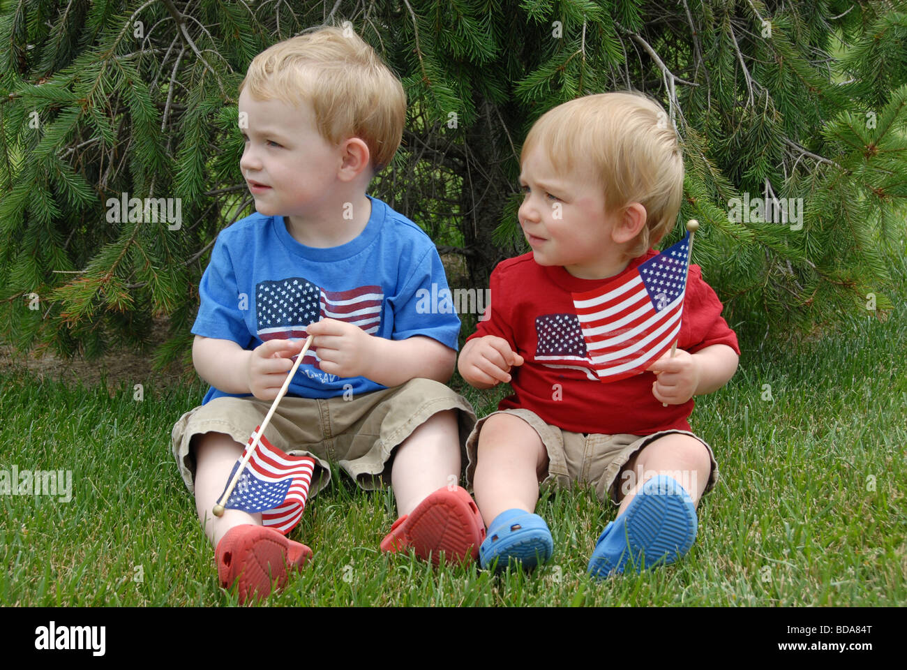 Two brothers celebrate the Fourth of July in there patriotic red, white, and blue outfits as they wave American flags. One is a Stock Photo