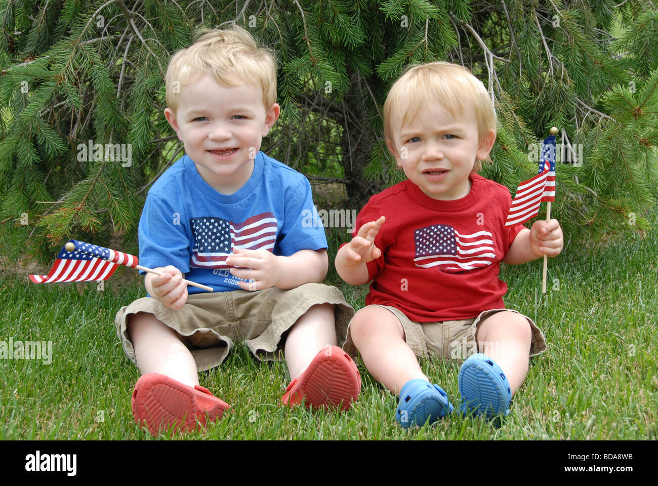 Two brothers celebrate the Fourth of July in there patriotic red, white, and blue outfits as they wave American flags. Stock Photo