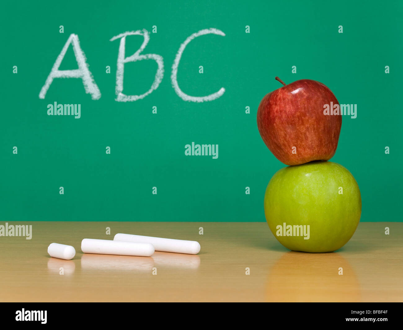 ABC written on a chalkboard. Some chalks and a red apple over a green one on the foreground. Stock Photo