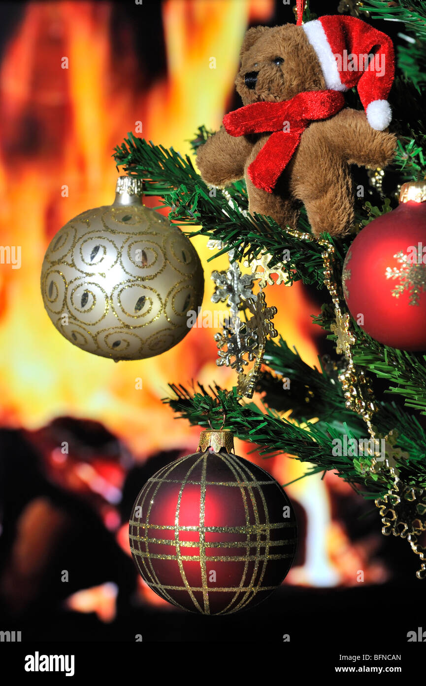 Teddy bear and bells hanging in Christmas tree in front of hearth / fireplace Stock Photo