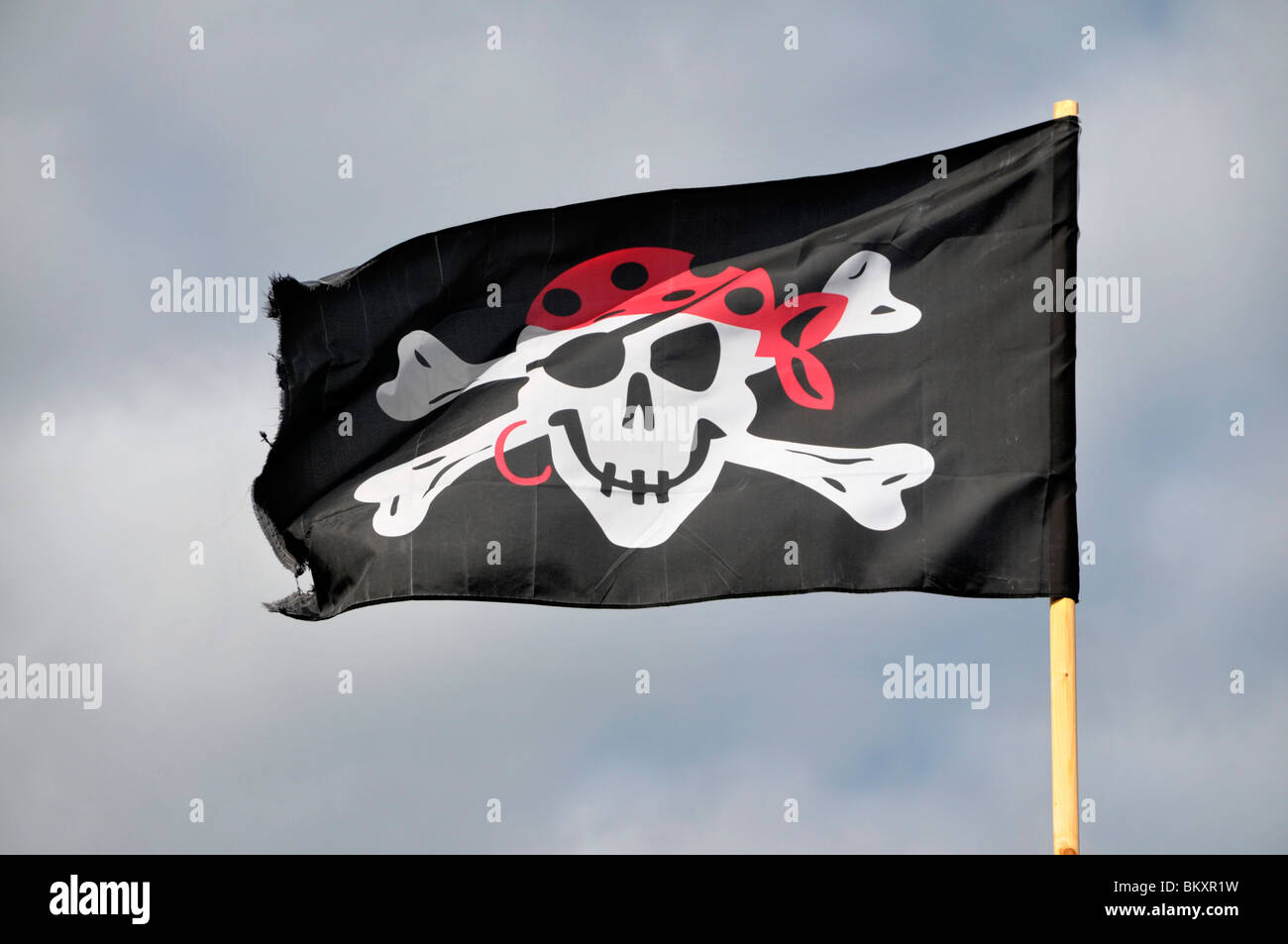 a black pirate skull and cross bone flag flying from a mast. Stock Photo