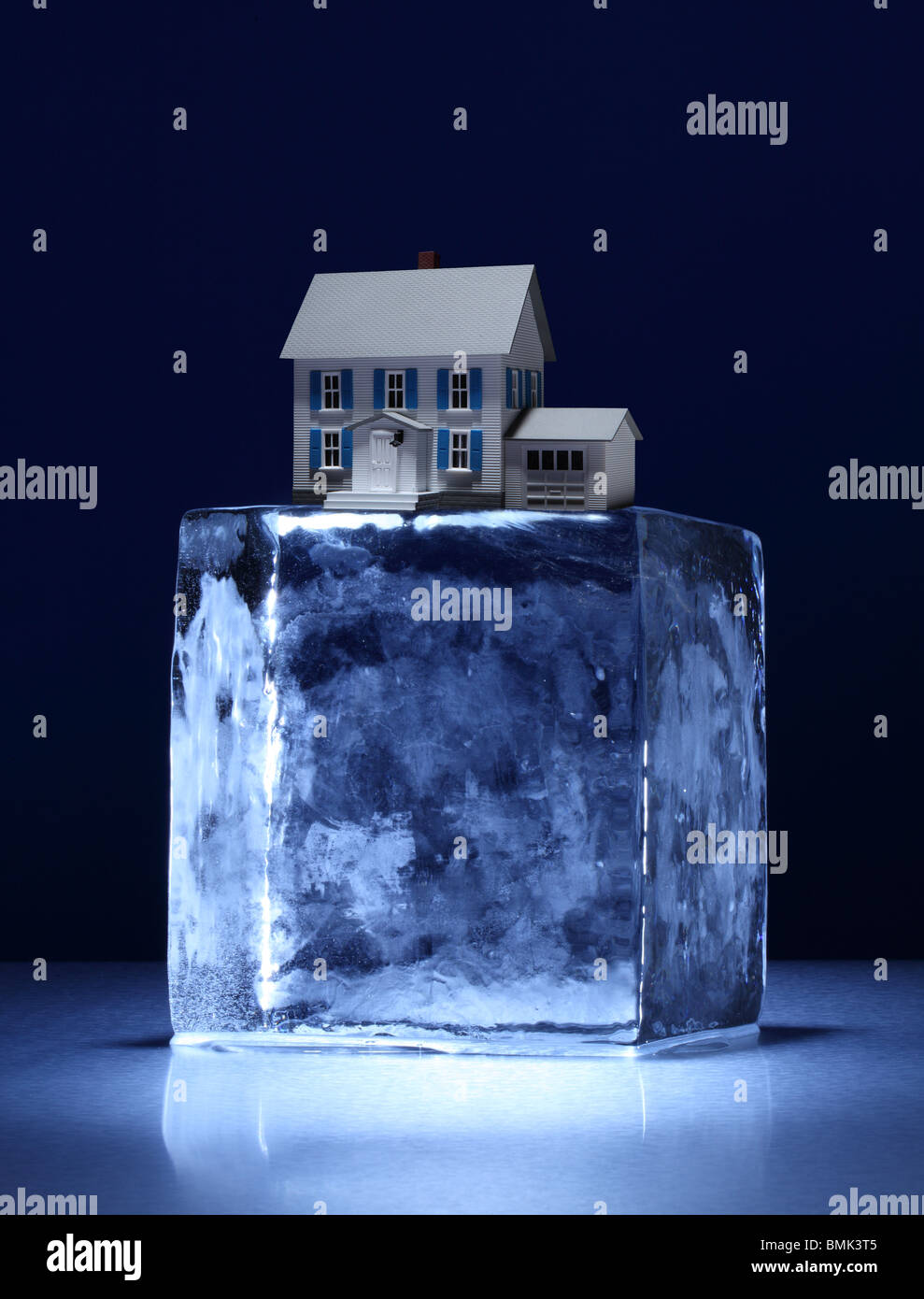 A frozen block of ice with a small model house on top on a metal surface Stock Photo