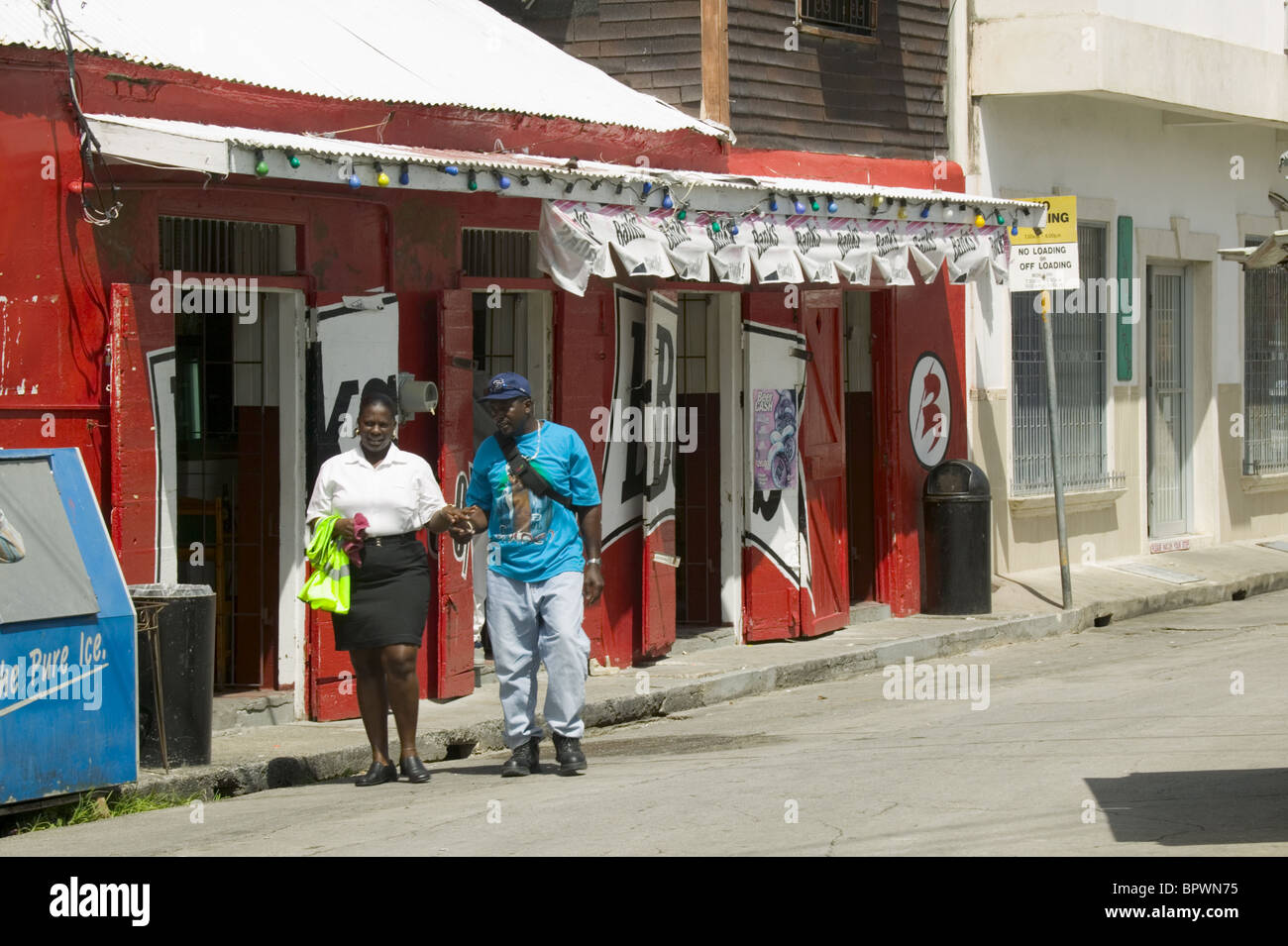 Couple passing a very bright red rum shop in Bridgetown, Barbados in the Caribbean Islands Stock Photo