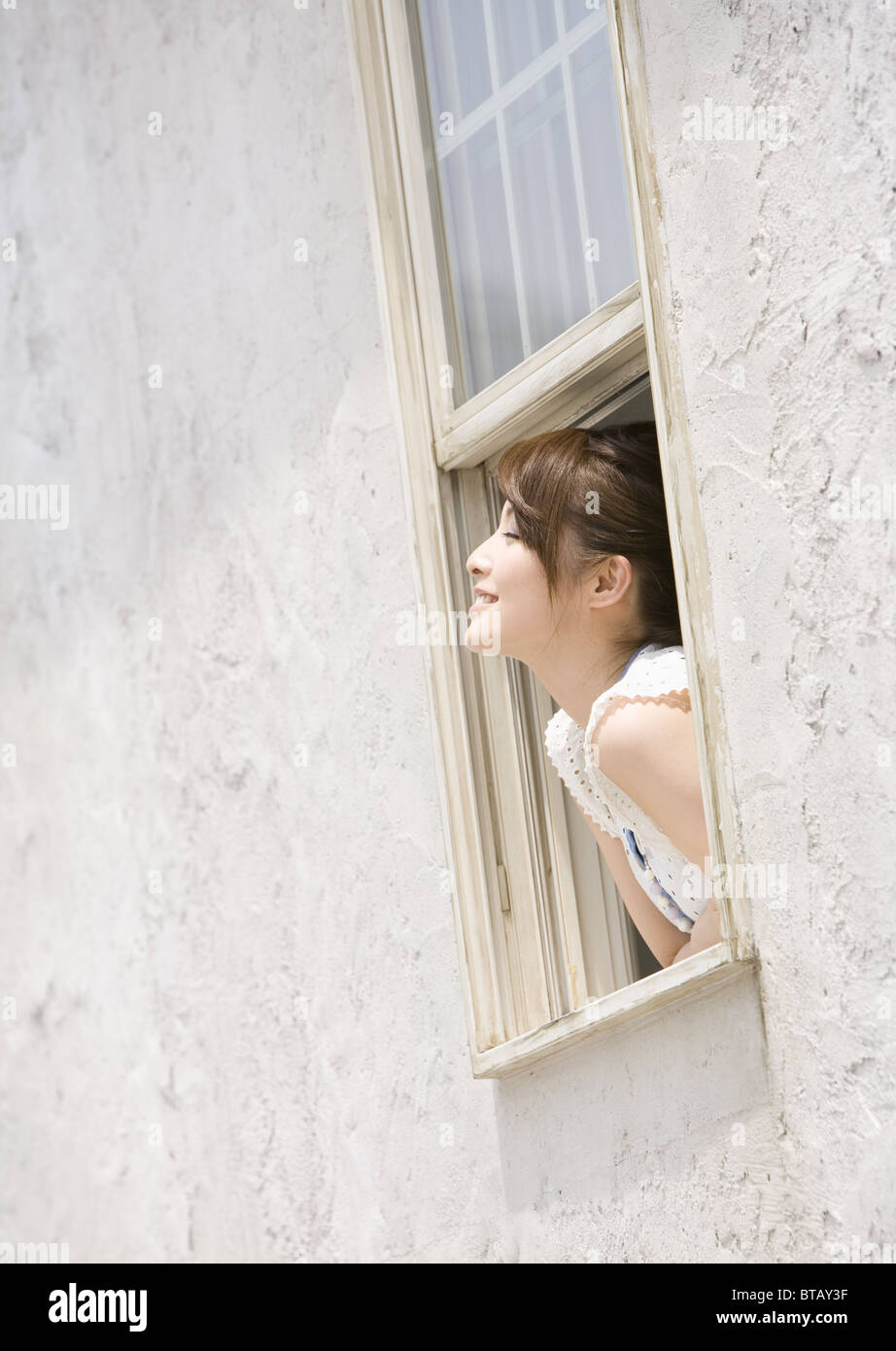 Young woman leaning out of window Stock Photo