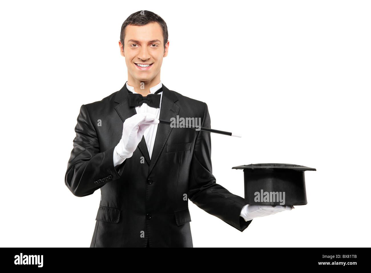 A magician in a black suit holding an empty top hat and magic wand Stock Photo