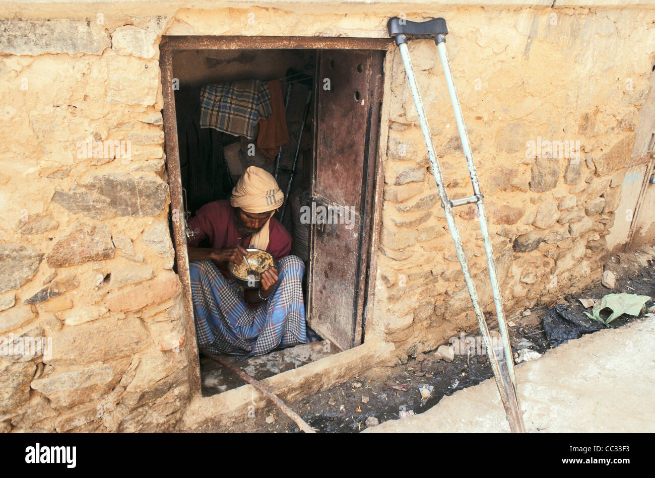 A poor man ( with a crutch) is eating in his small room that is overlooking the street ( India) Stock Photo