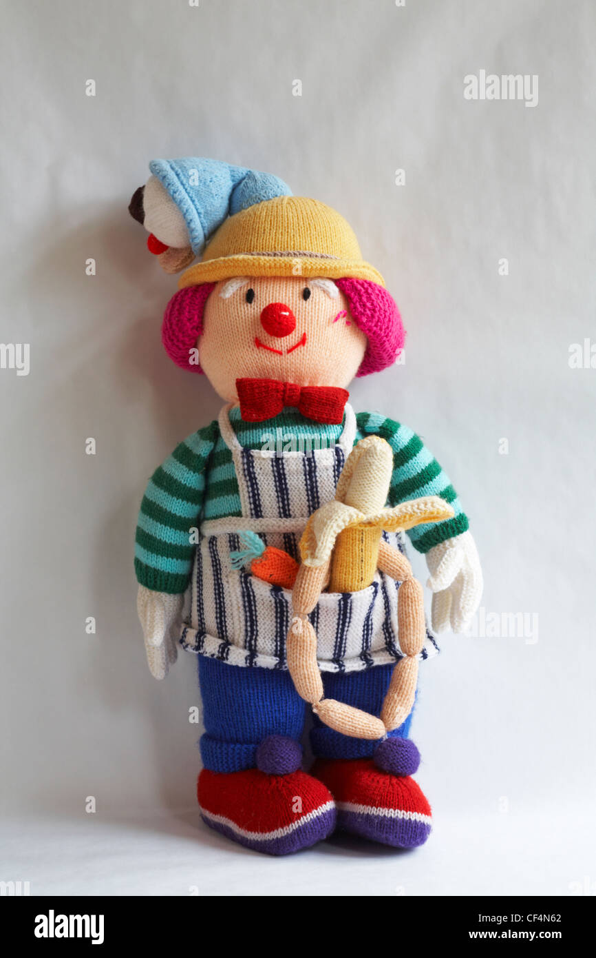 knitted doll, knitted toy with icecream cornet on head and carrot, banana and string of sausages in apron pocket isolated on white background Stock Photo