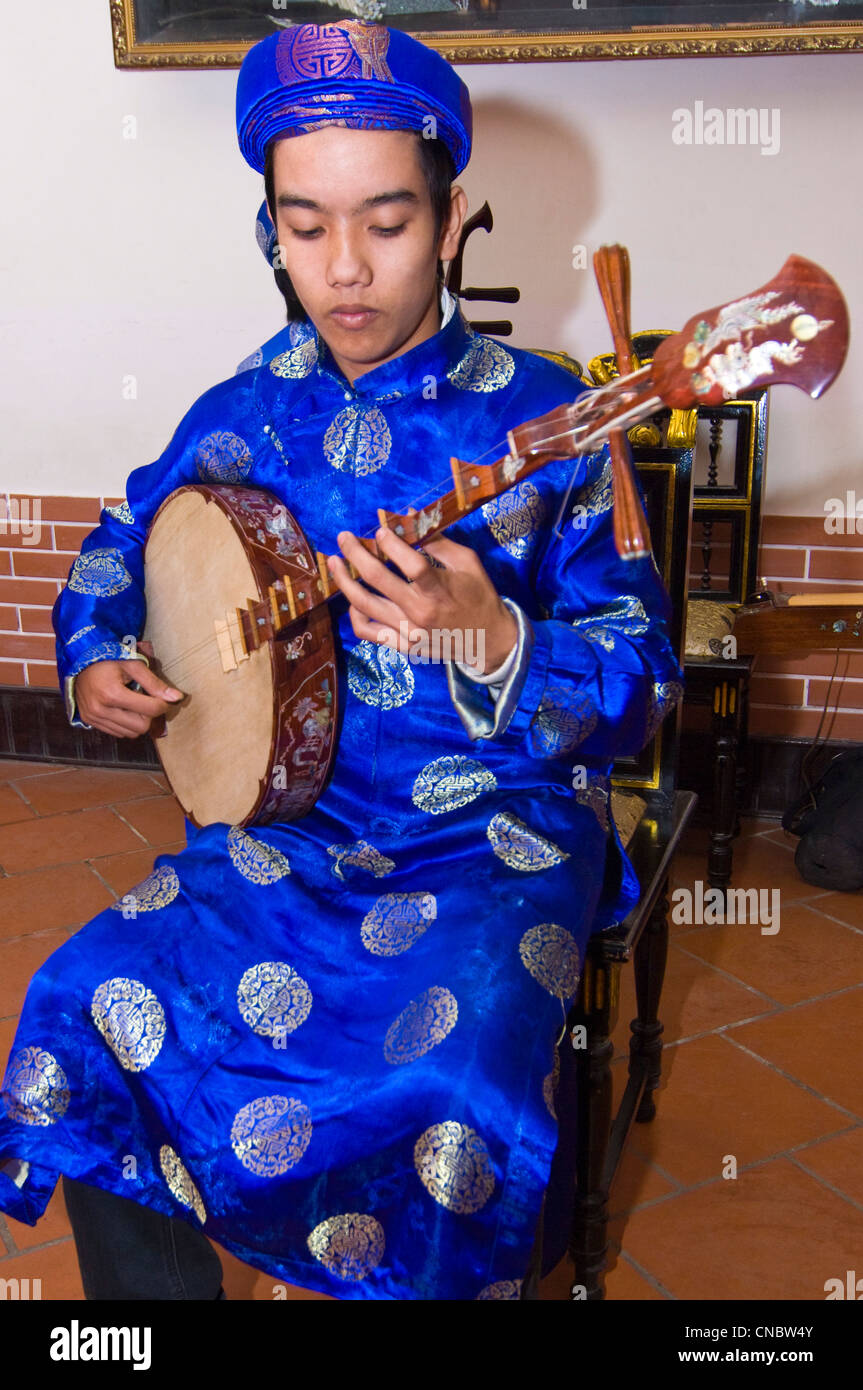 Vertical close up view of traditional Vietnamese musician playing the dan nguyet or Full Moon lute guitar in costume. Stock Photo