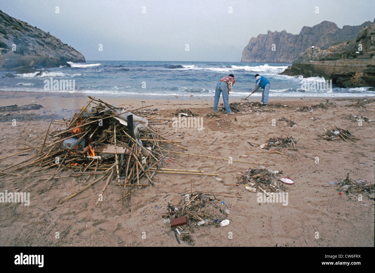 two men collecting and burning flotsom and garbage at the beach, Spain, Spain, Balearen, Majorca Stock Photo