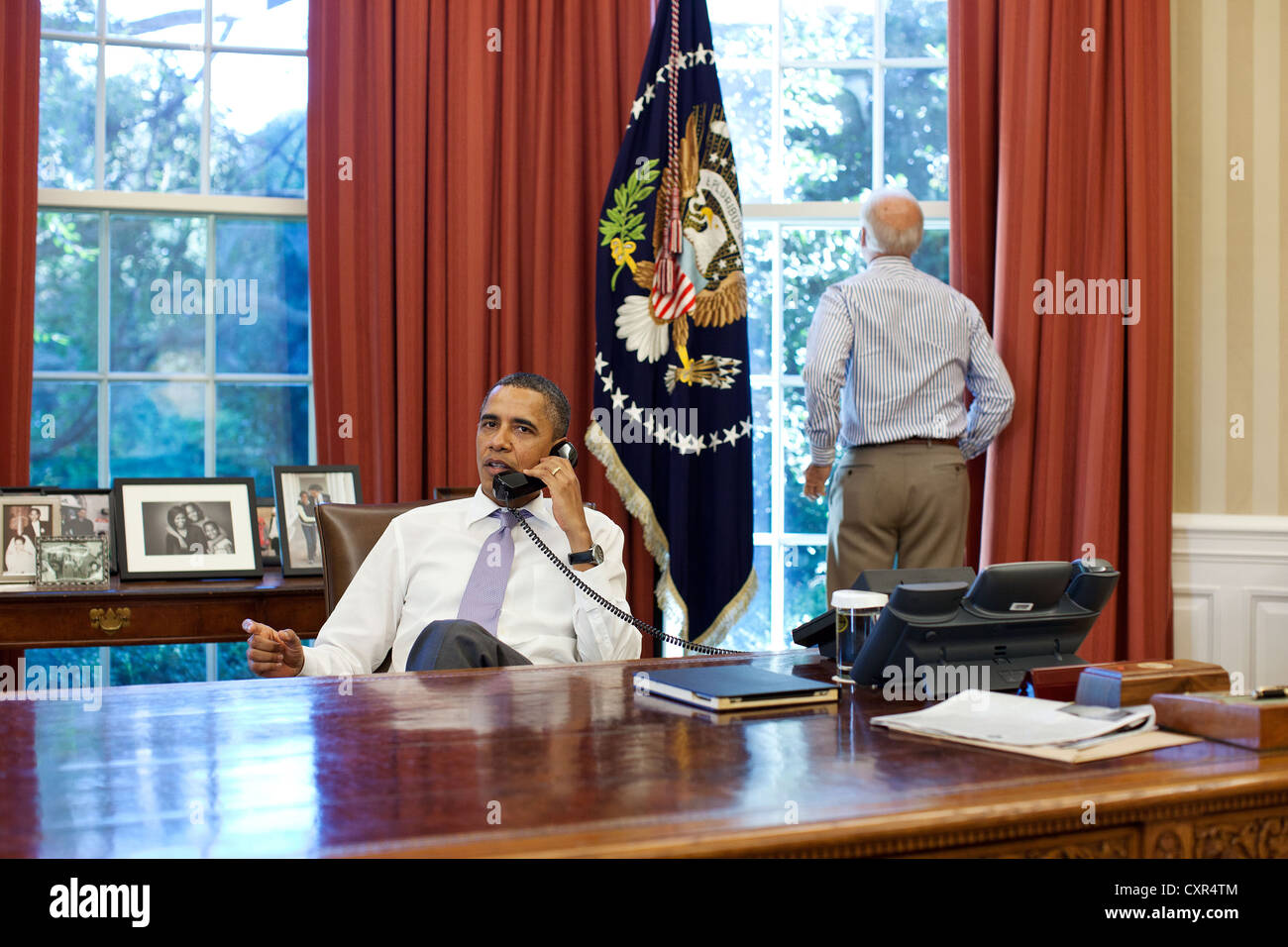 US Vice President Joe Biden looks out the window as President Barack Obama talks on the phone with House Speaker John Boehner in the Oval Office to discuss ongoing efforts in the debt limit and deficit reduction talks, Sunday, July 31, 2011. Stock Photo