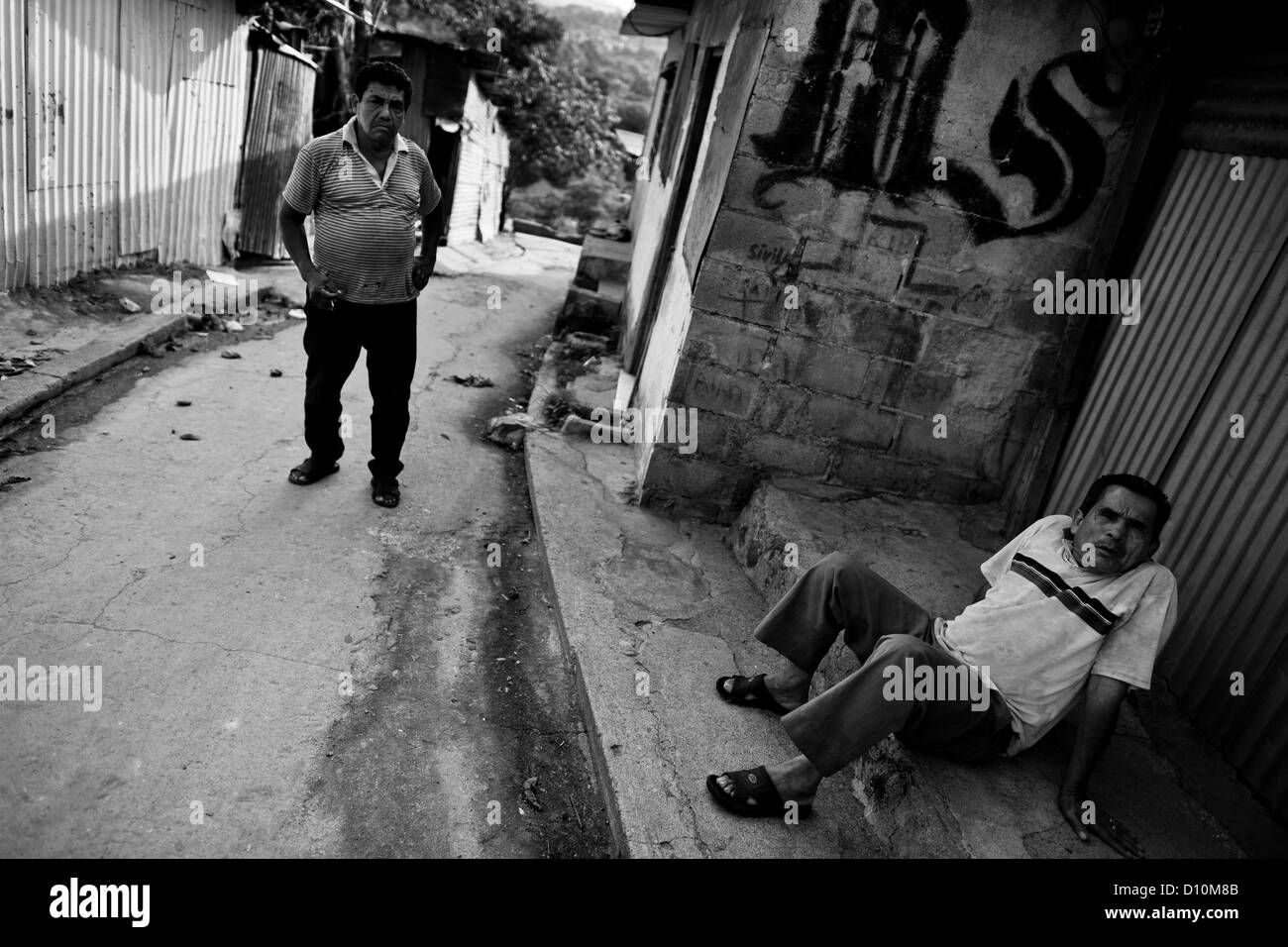 An old man sits in front of the gang graffiti painted on the wall in the Mara Salvatrucha gang neighborhood in El Salvador. Stock Photo