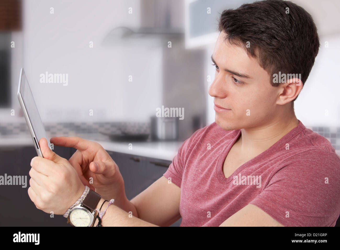 Young man using a digital tablet, looking at the screen or monitor. Situated in a modern kitchen. Stock Photo