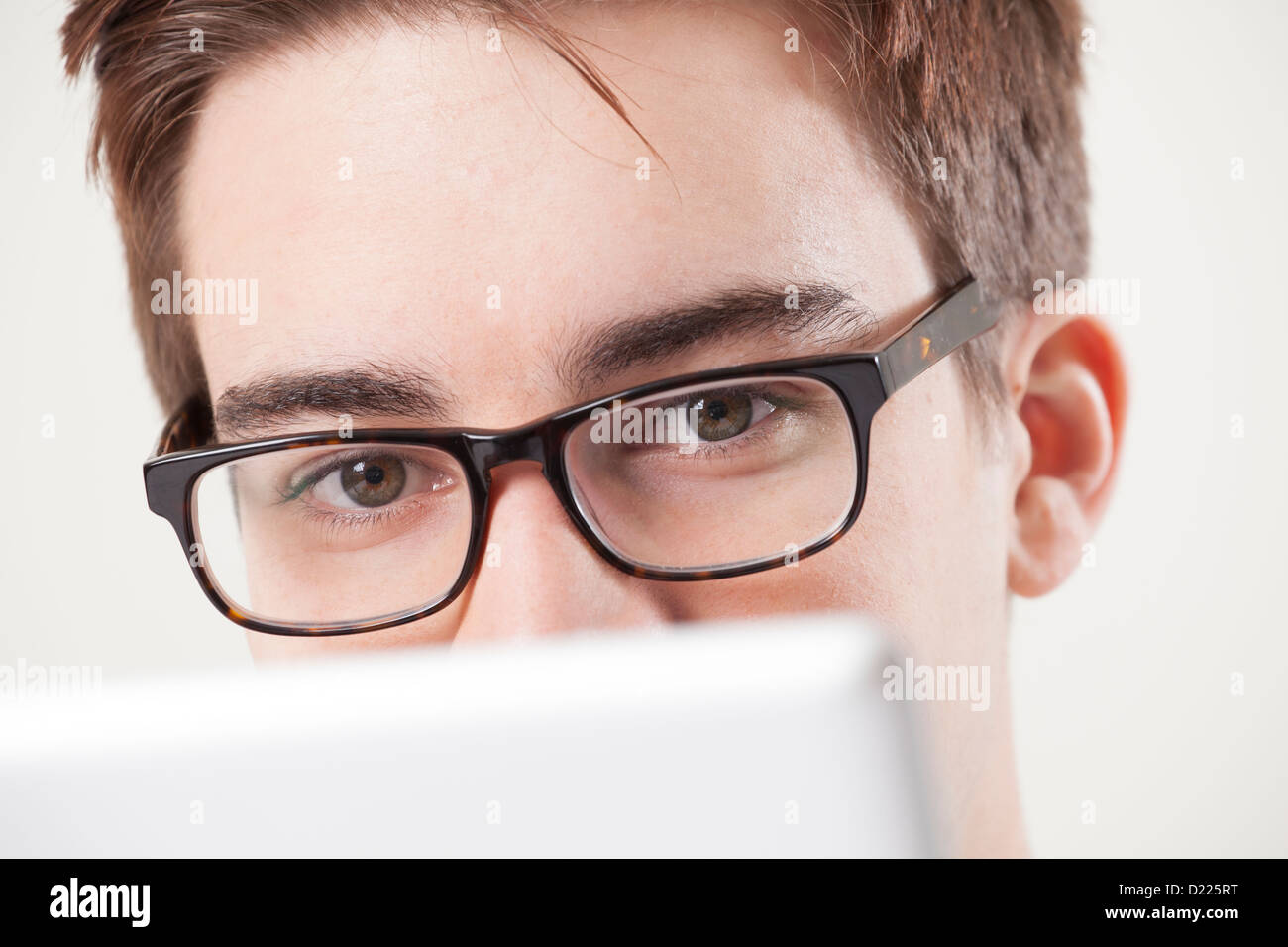 Young male wearing glasses looking to camera, using a laptop or digital tablet. Close up on eyes. Stock Photo