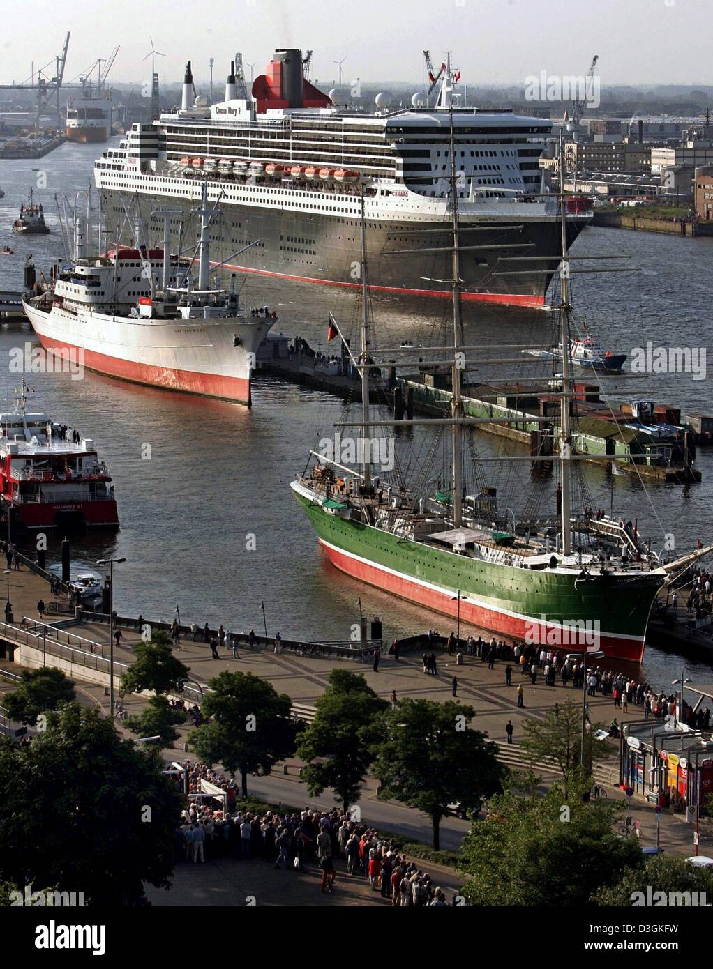 (dpa) - Trailed by several smaller boats leaves the world's largest and most expensive cruise ship, the Queen Mary 2, the harbour in Hamburg, Germany, Tuesday 20 July 2004. After spending a day in the northern German port city and impressing tens of thousands of onlookers, the ocean liner now heads to his home port of Southampton, United Kingdom. Stock Photo