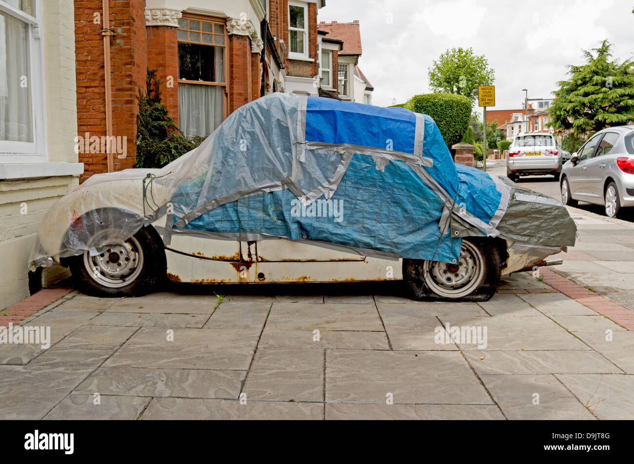 A clapped-out old car beneath a patched-up cover. Stock Photo