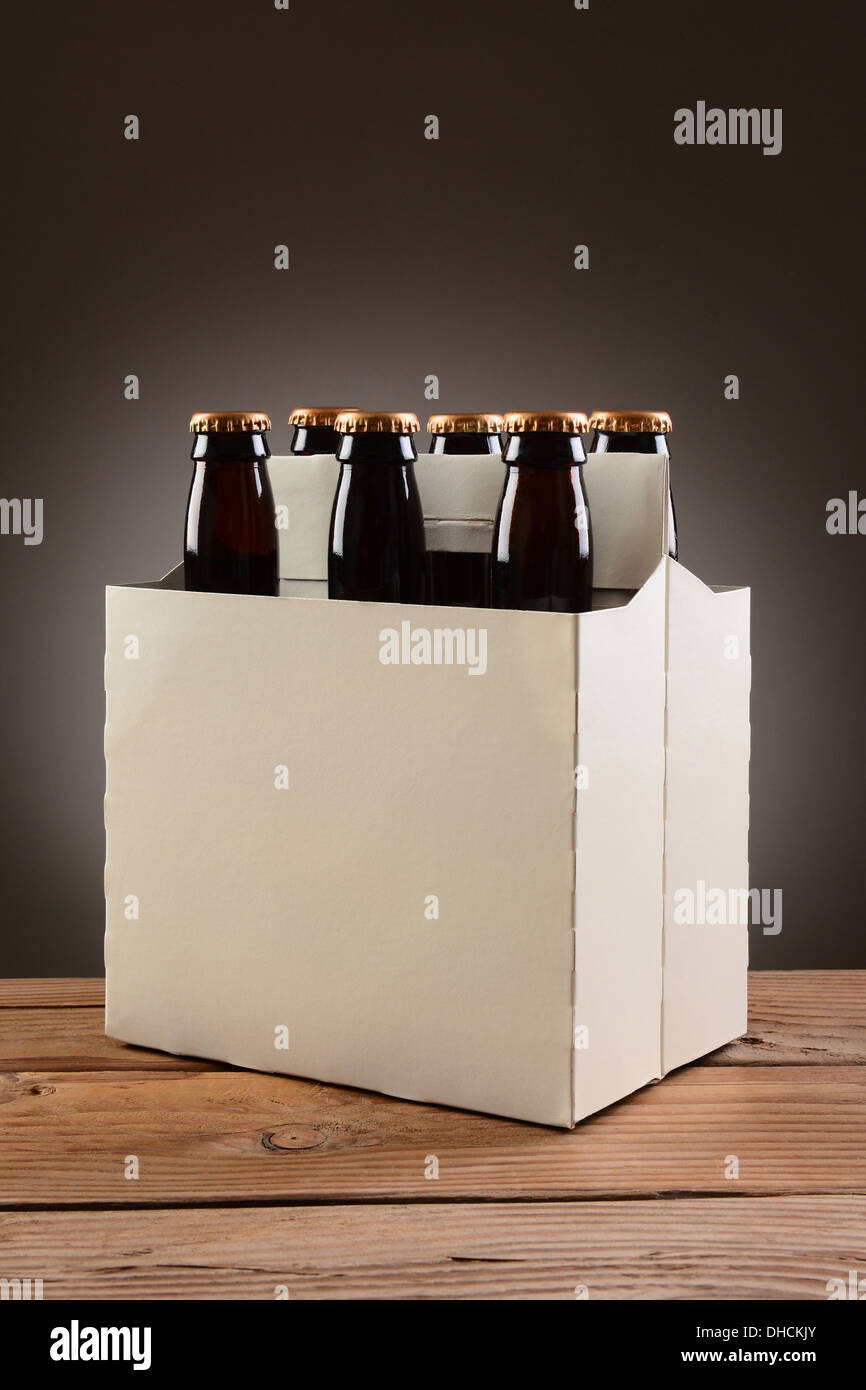 Closeup of a six pack of brown beer bottles on a rustic wooden table. Vertical format with a light to dark gray spot background. Stock Photo