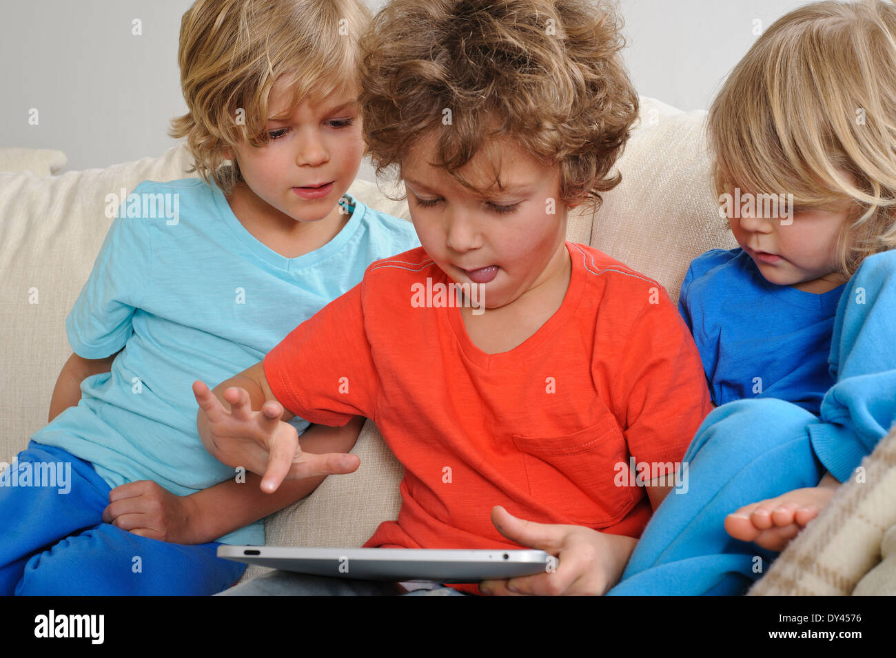 An 8-9 year old is playing a game on a touch screen tablet. His younger brothers are watching every move intently Stock Photo