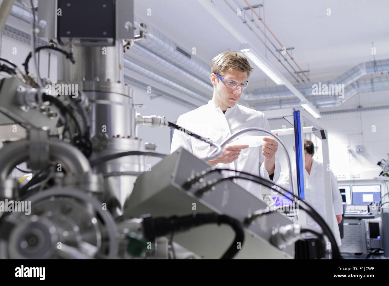 Scientist standing in analytical laboratory with scanning electron microscope in foreground Stock Photo