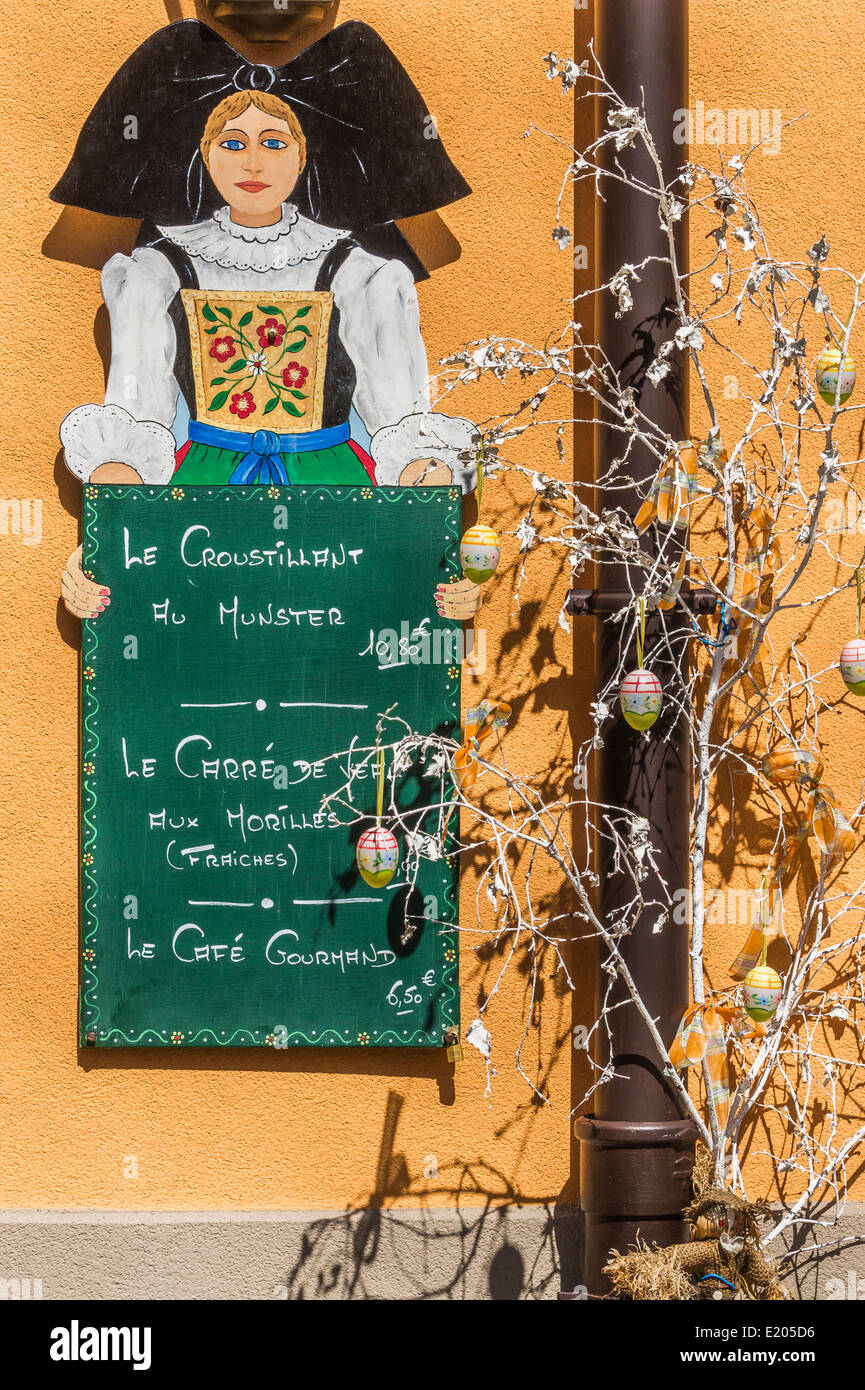 sign of a restaurant showing a young woman in traditional alsatian garb and advertising alsatian culinary specialities Stock Photo