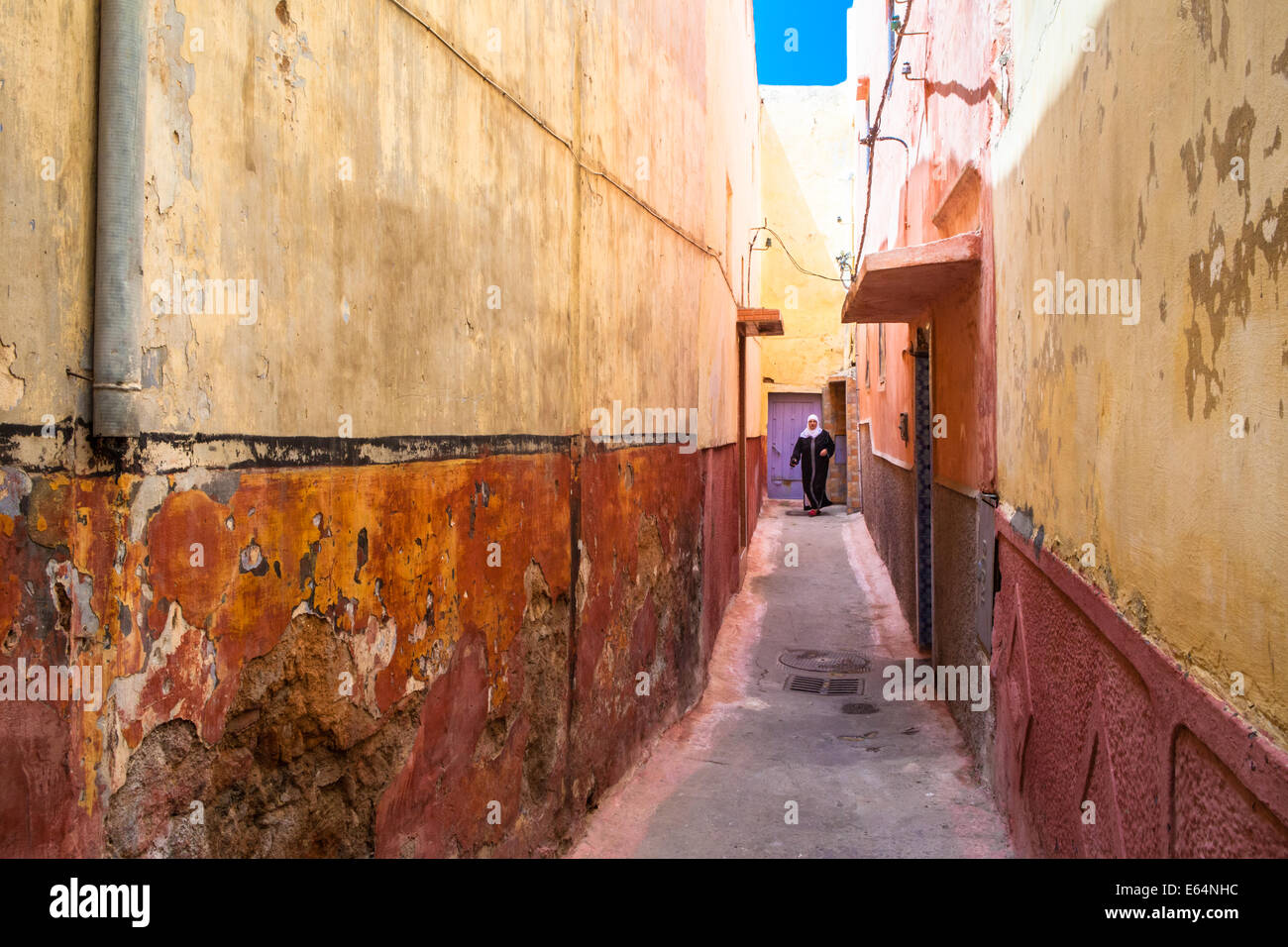 Arab Muslim woman, wearing a headscarf and a black djellaba, in a colorful alley of the old medina of Salé, near Rabat, Morocco. Stock Photo