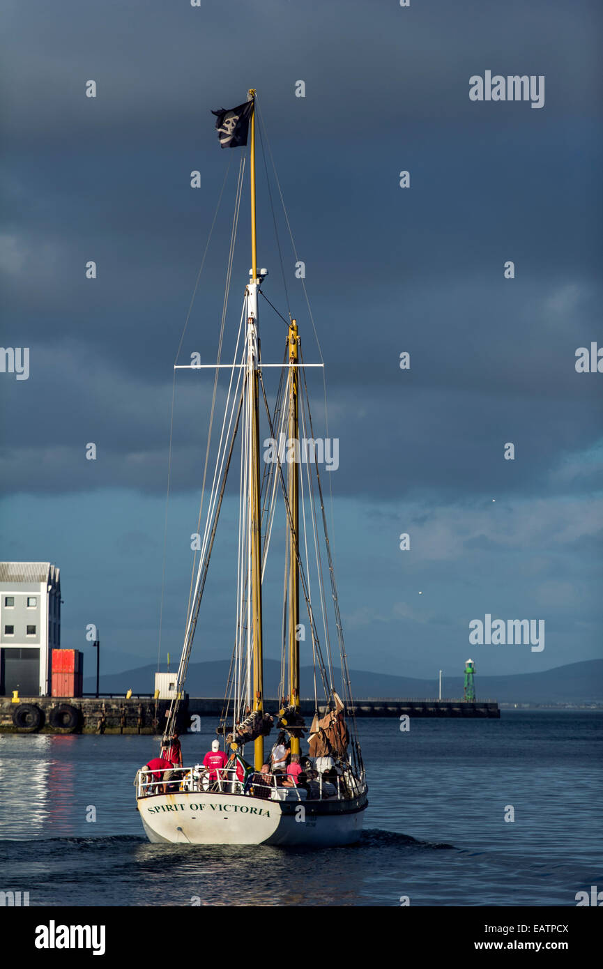 A yacht heads to sea from a harbor flying a pirate flag on it's mast. Stock Photo