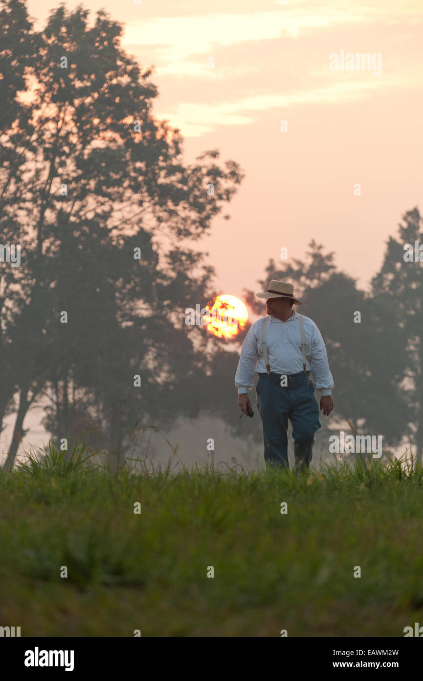 A man dressed in civil war garb walks through a field at sunrise. Stock Photo