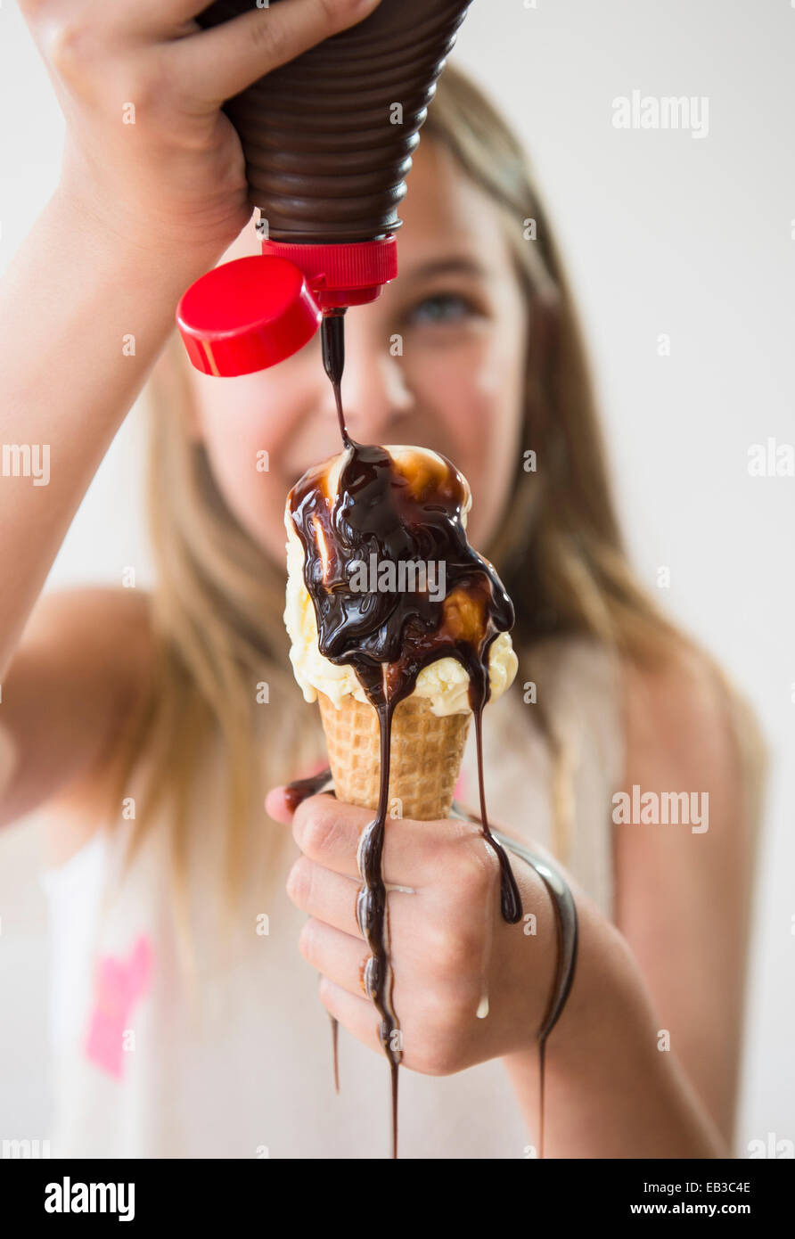 Messy Caucasian girl pouring chocolate syrup on ice cream cone Stock Photo