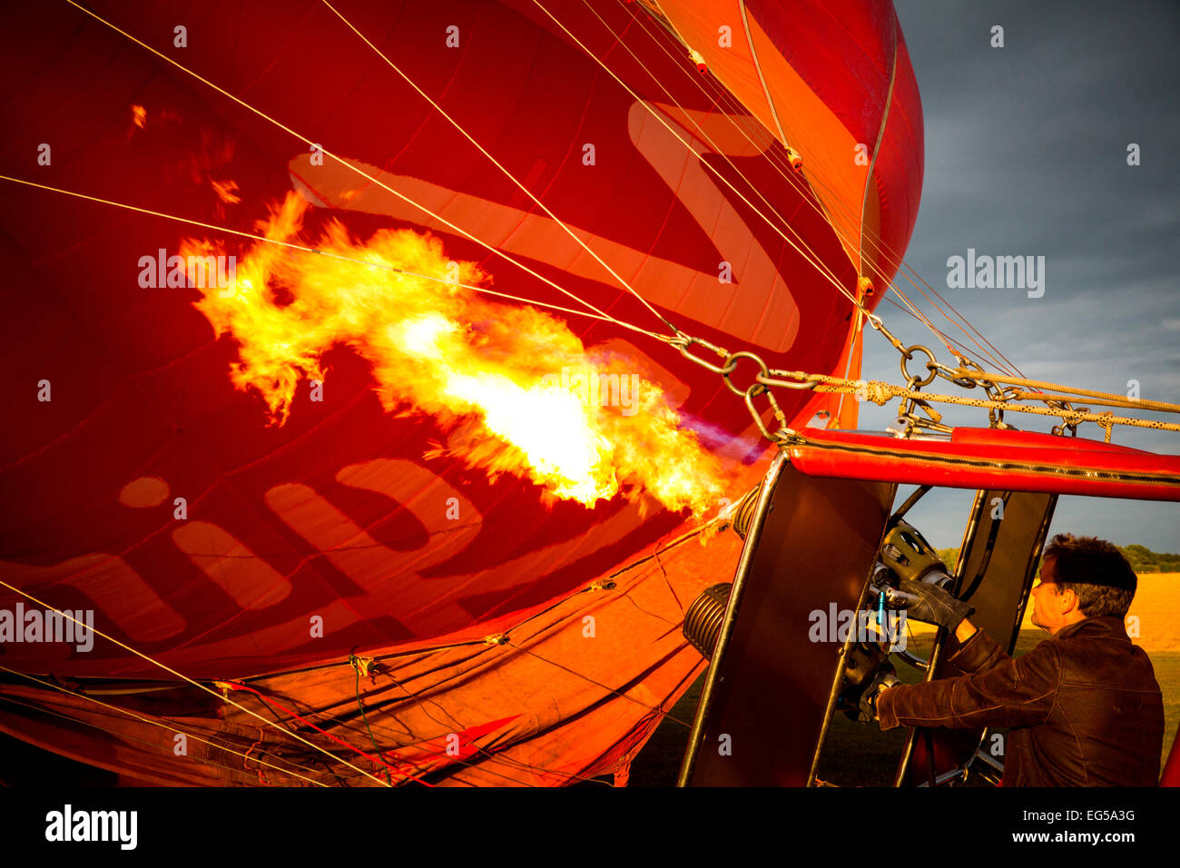 Man controlling gas burner flames inflating red hot air balloon, South Oxfordshire, England Stock Photo