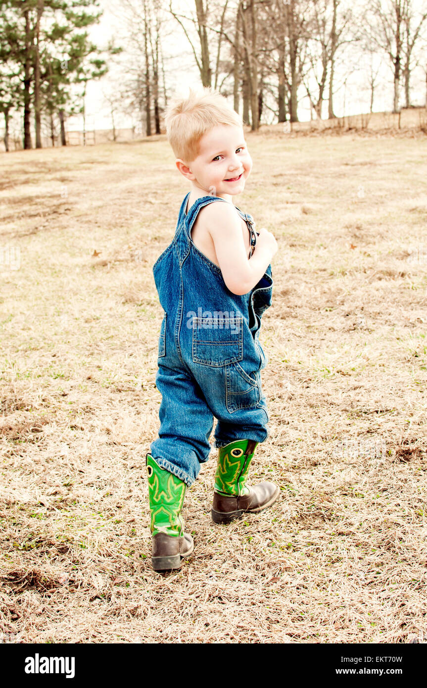 boy in denim coveralls and boots walks in the country Stock Photo