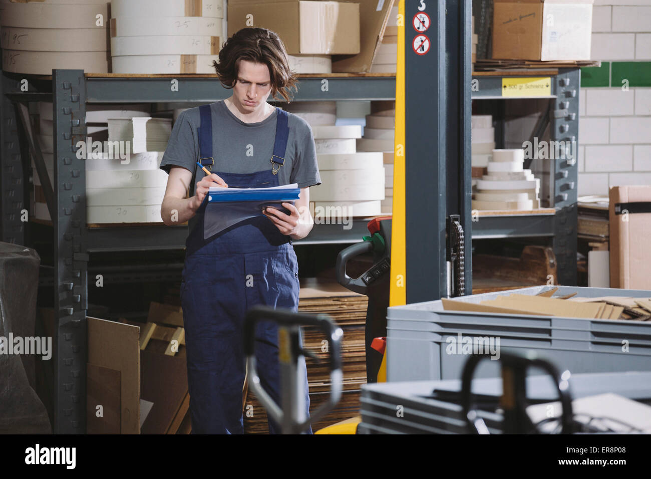 Young manual worker in coveralls writing notes in warehouse Stock Photo