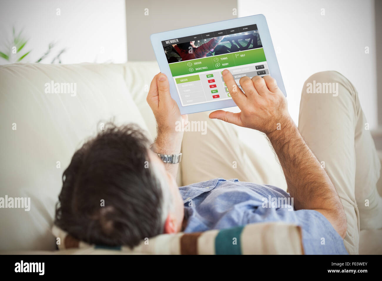 Composite image of man laying on sofa using a tablet pc Stock Photo