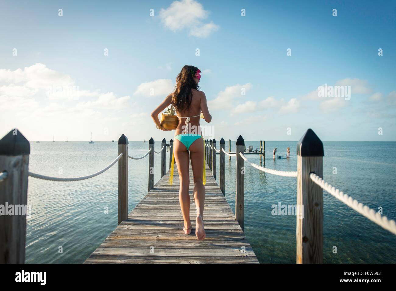 Rear view of young woman on sea pier carrying bowl of fruit, Islamorada, Florida, USA Stock Photo