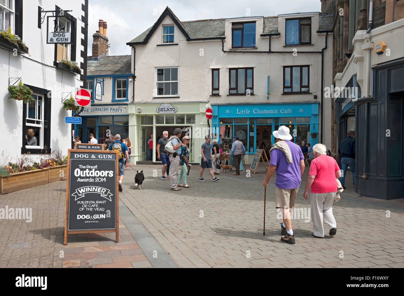 People senior couple tourists visitors walking town centre shops shop street in summer Keswick Cumbria Lake district England UK GB Great Britain Stock Photo