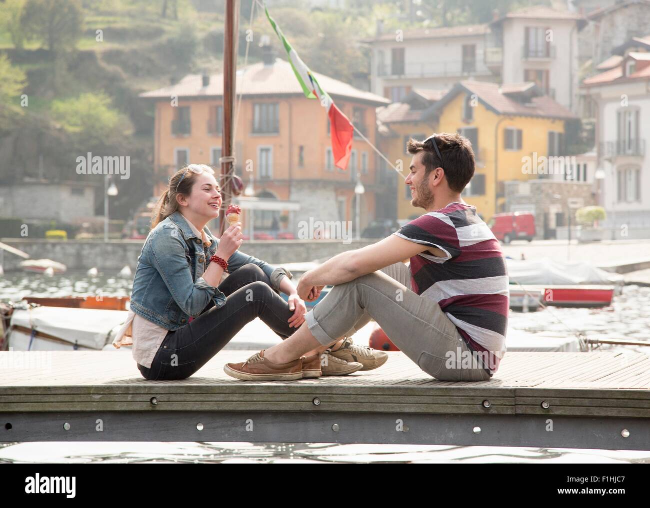 Couple sitting on pier eating ice cream cone at lake Mergozzo, Verbania, Piemonte, Italy Stock Photo