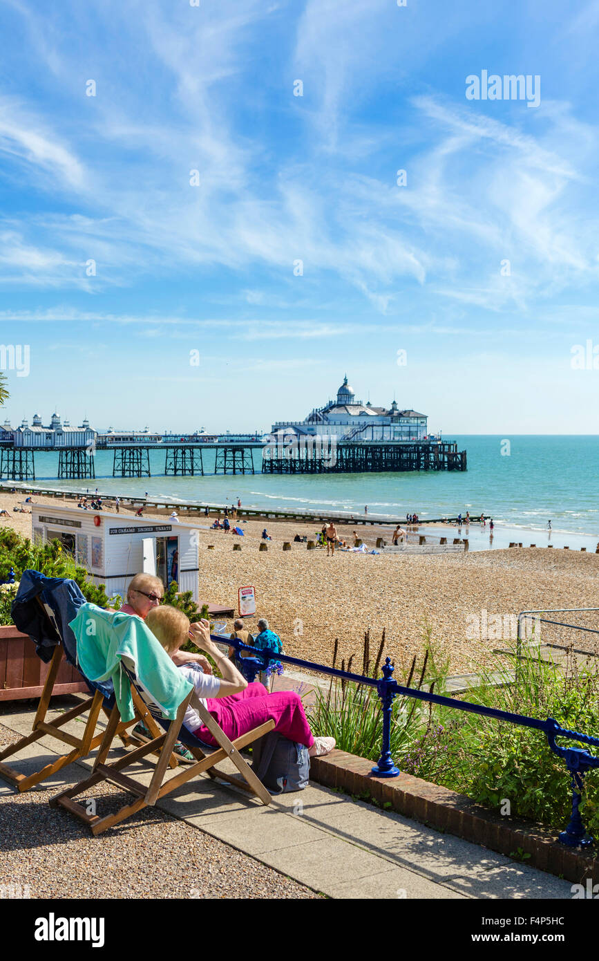 Two elderly women sitting on the promenade with the beach and pier behind, Grand Parade, Eastbourne, East Sussex, England, UK Stock Photo