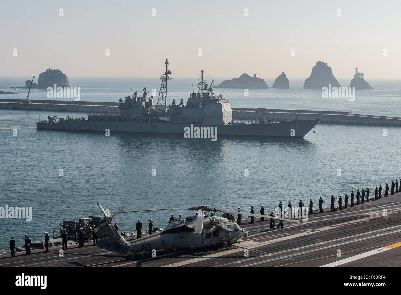 The U.S. Navy Sailors stand at parade rest while manning the rails aboard the Nimitz-class nuclear-powered supercarrier USS Ronald Reagan alongside the Ticonderoga-class guided-missile cruiser USS Chancellorsville as they depart the Busan harbor after a goodwill port visit November 4, 2015 in Busan, South Korea. Stock Photo