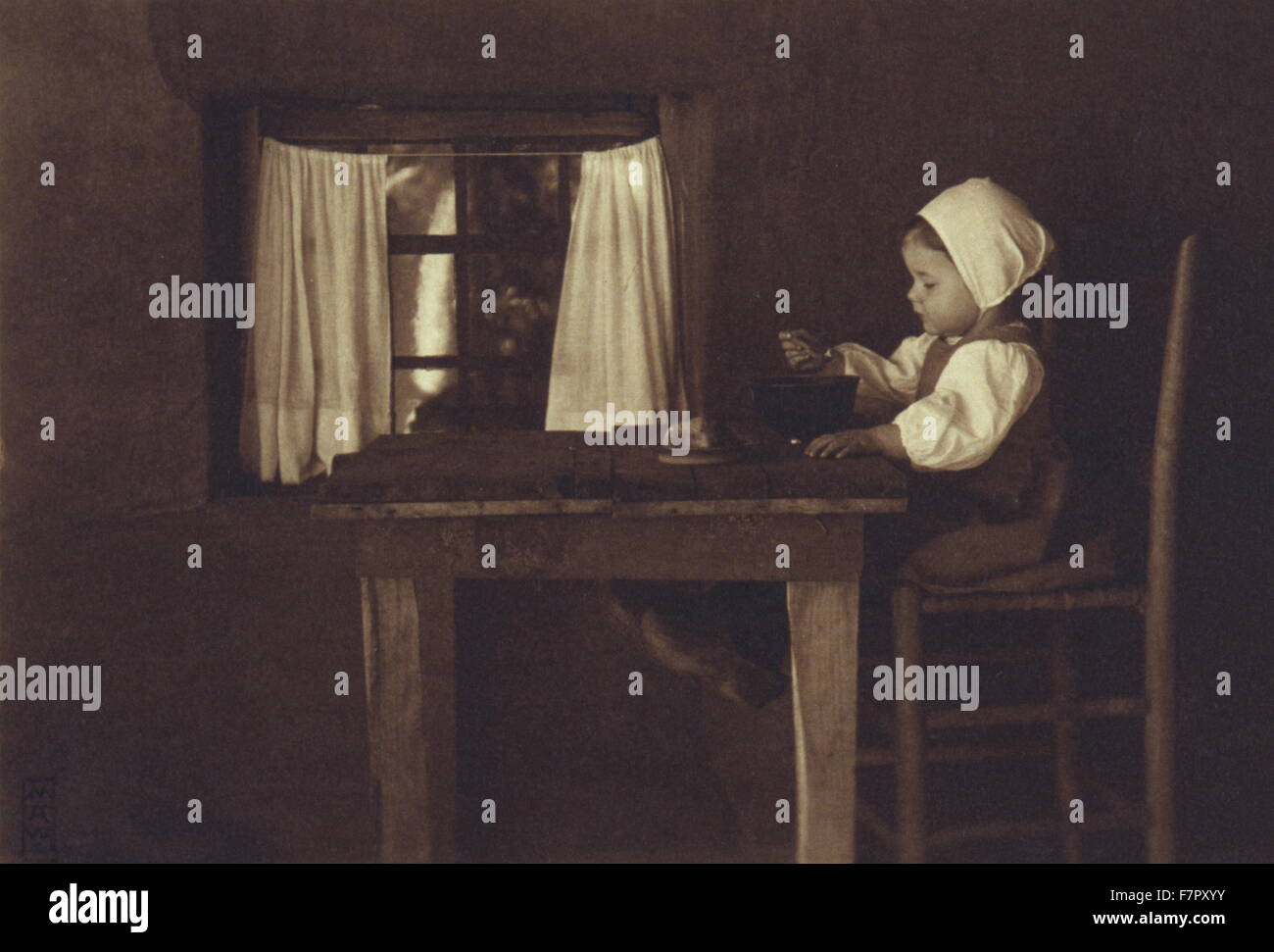 Hunger ist der beste Koch. photograph dated 1898 by Myra Albert Wiggins, 1869-1956;shows a little girl, wearing a cap and wooden shoes, seated on a high chair at a wooden table, eating from a bowl. Stock Photo