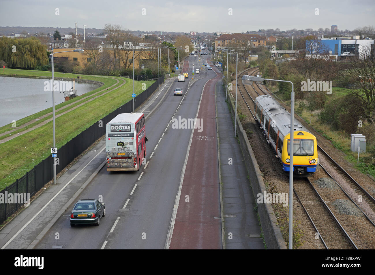 View of Forest Road in North London showing Overground train, double deck bus, cars, bus lane and reservoir to the left Stock Photo