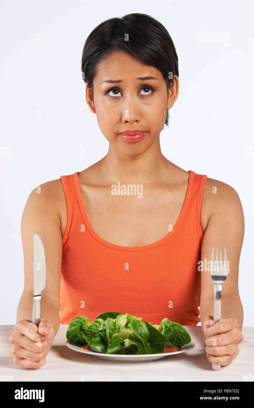 Unhappy Woman Sitting In Front Of Lettuce Leaves On Plate Stock Photo