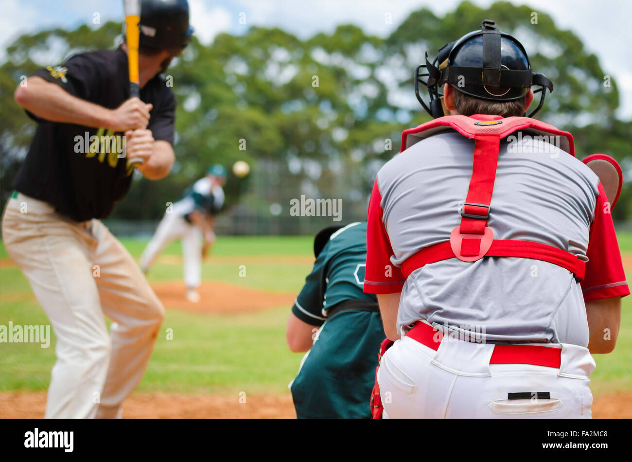 Baseball pitcher throwing ball to batter watched by Umpire and Catcher. Stock Photo