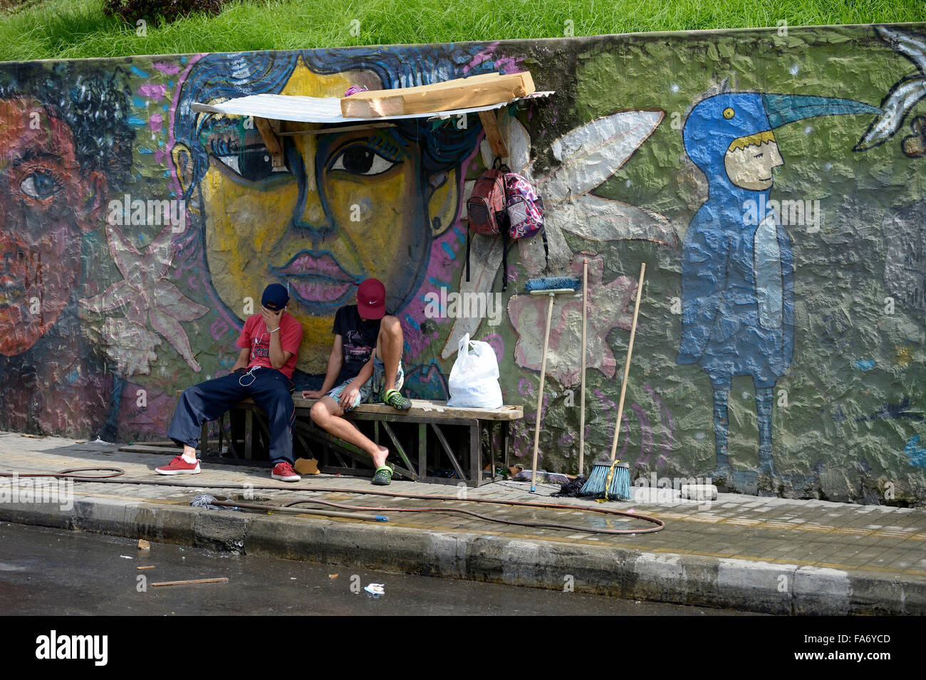 Young gang members sitting in front of graffiti wall, Comuna 8 slum, Medellin, Antioquia Department, Colombia Stock Photo