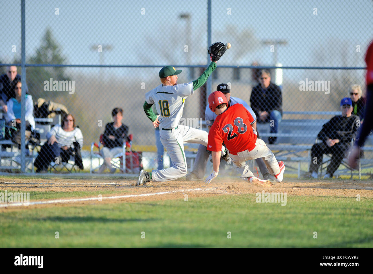 High school base runner scoring from third base on a wild pitch ahead of a throw and tag from the pitcher who covered the plate. USA. Stock Photo