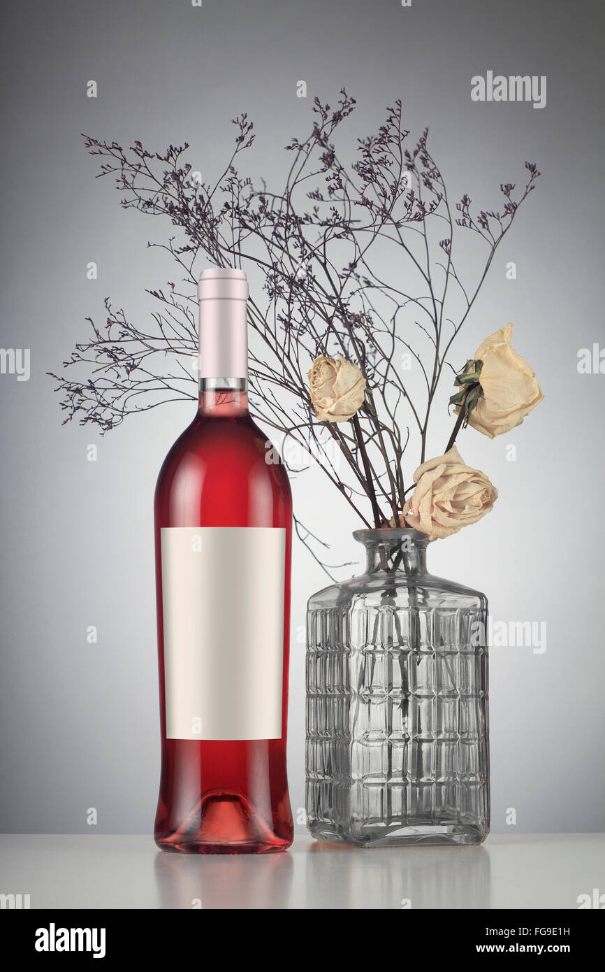 Rose wine bottle with label mockup to withered white roses in a vase. Stock Photo