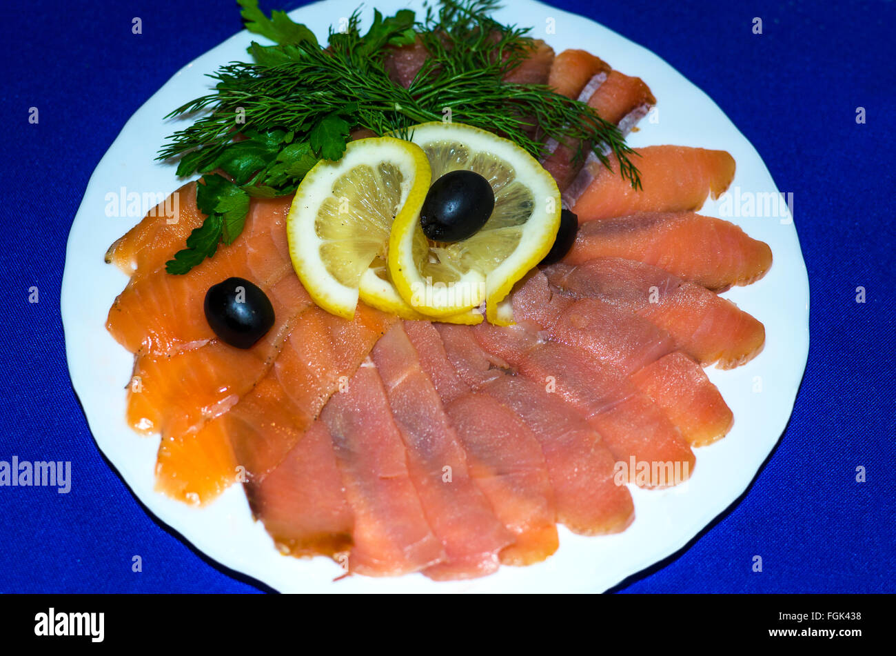 Red fish is cut by slices on a plate,red,fish,slices,is cut,white,a plate,blue,a background,a lemon,a product,food,snack,fish Stock Photo