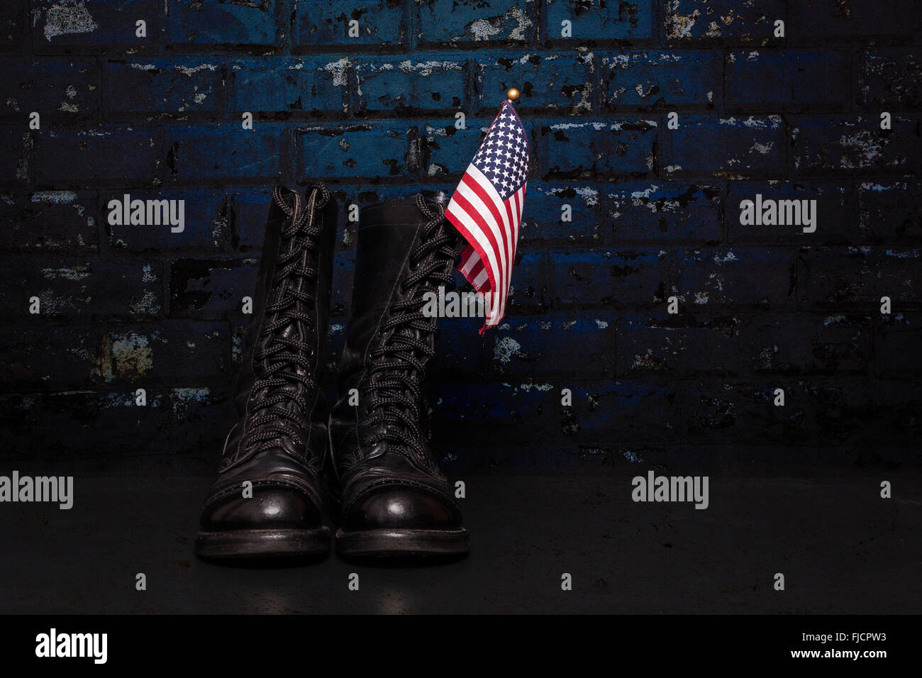 A pair of combat boots with a small American Flag on a blue brick background. Stock Photo